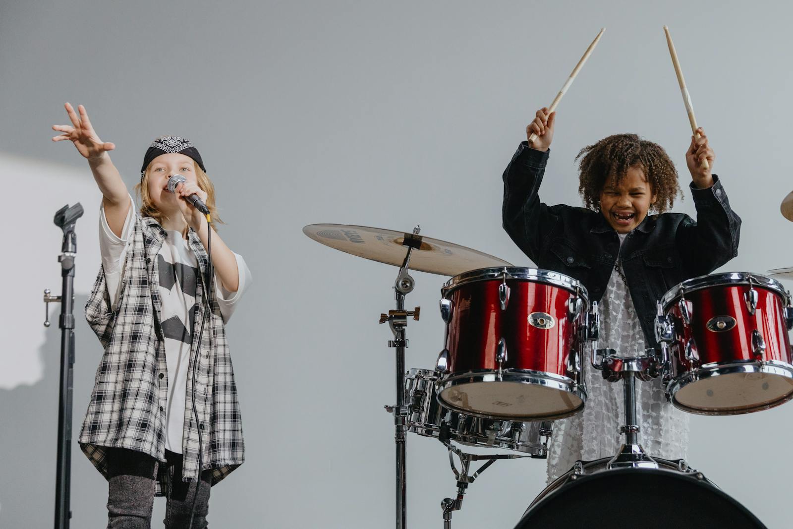 Photograph of a Kid Playing the Drums Beside a Child Singing